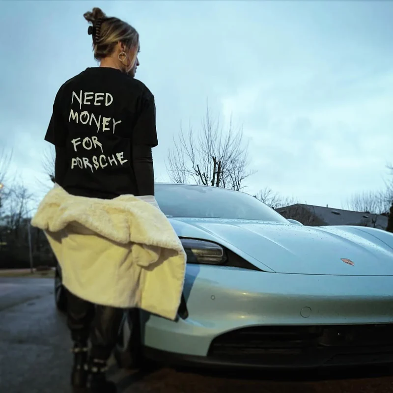Customer wearing Need Money For Porsche tee next to a Porsche Taycan