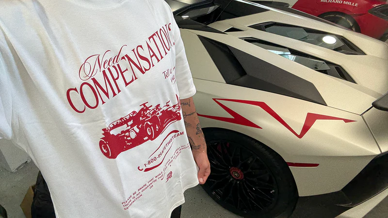 Customer wearing Need Compensation tee next to a Lamborghini